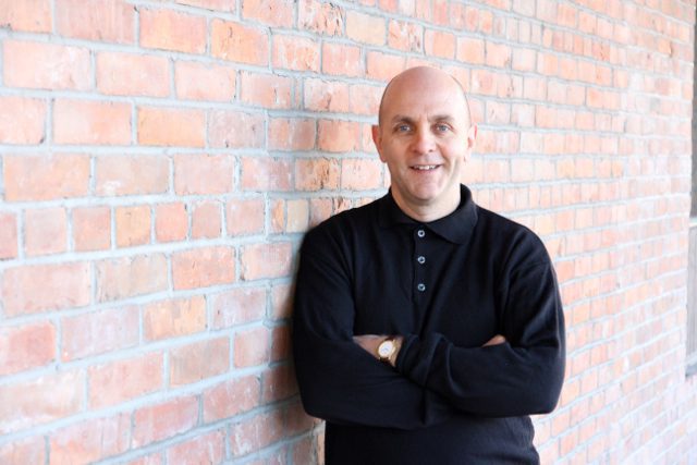 The President of Next Stage Consulting, Larry, stands in front of a brick wall